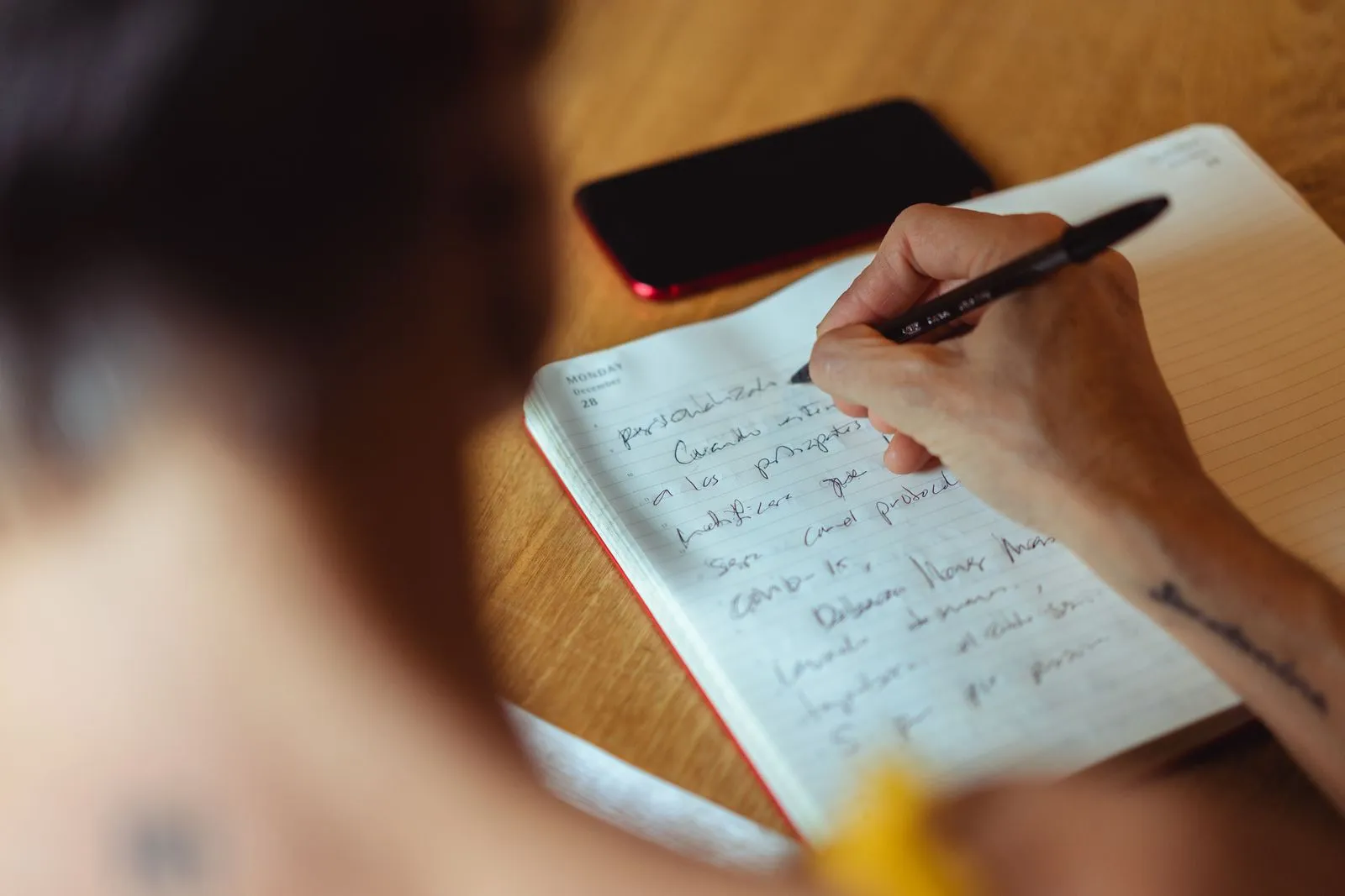 Person writing in a notebook at a desk with a phone set aside