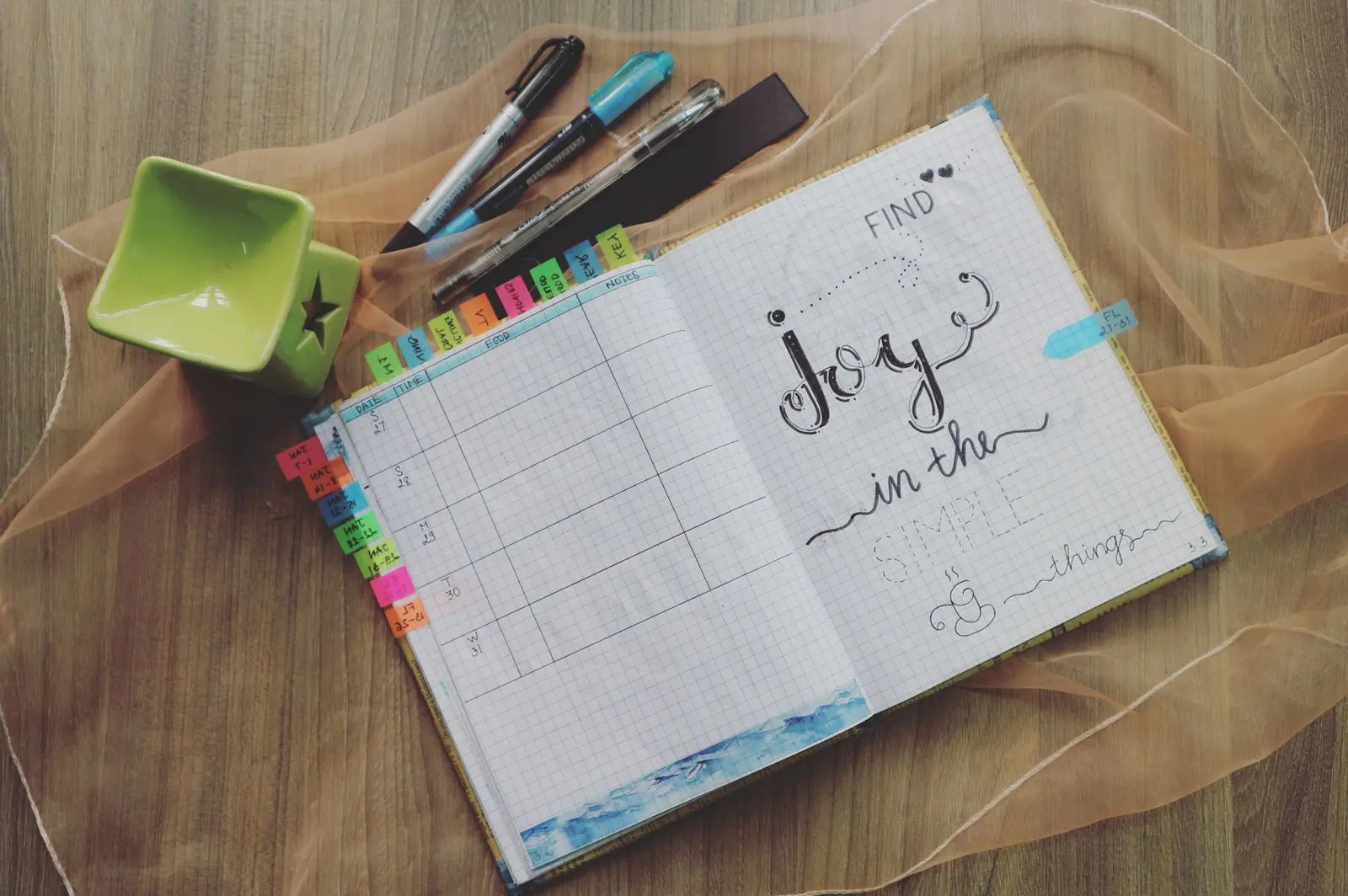 Flat lay of an open bullet journal with colorful tabs and pens on a wooden desk
