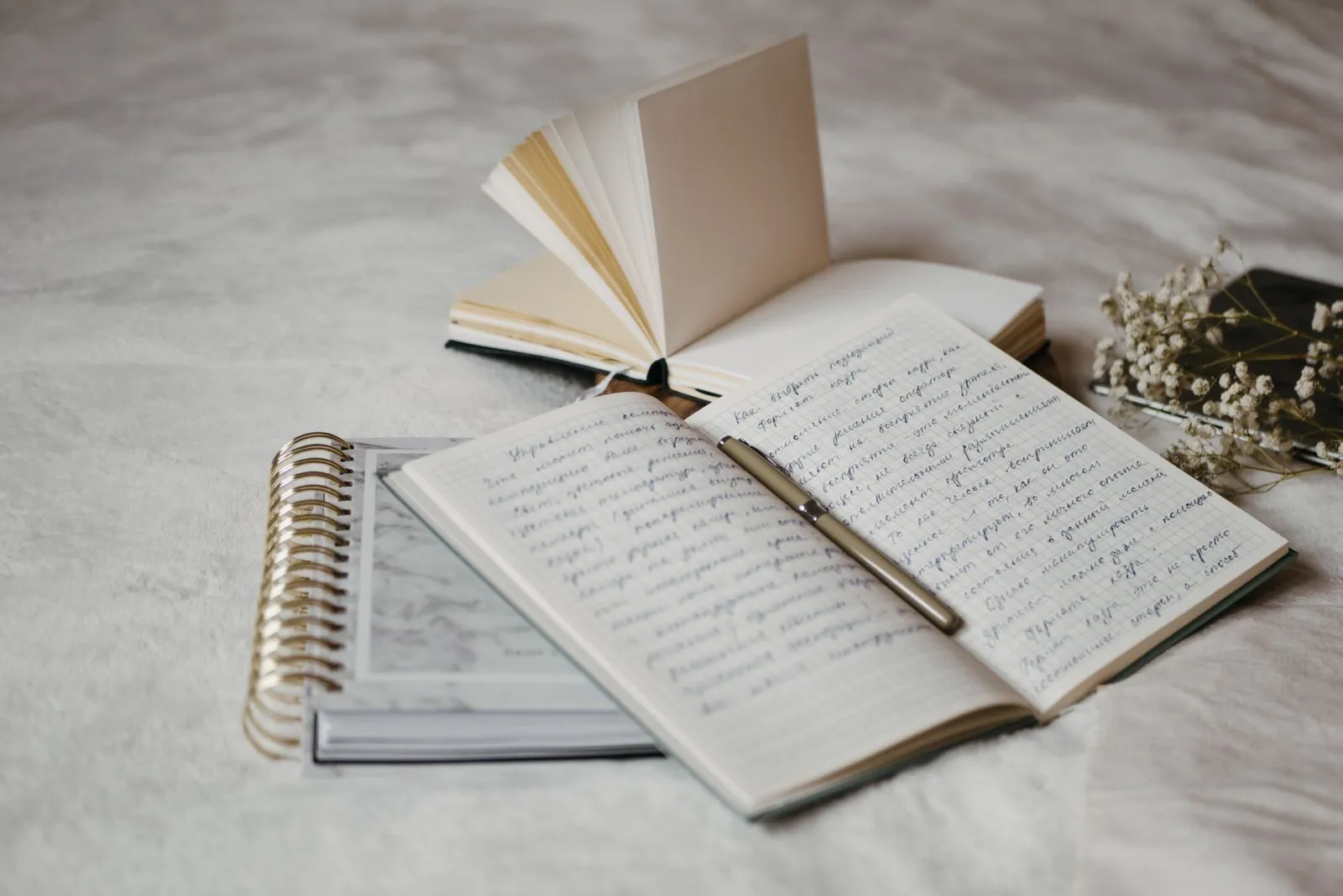 An open notebook and pen on a bed beside dried flowers