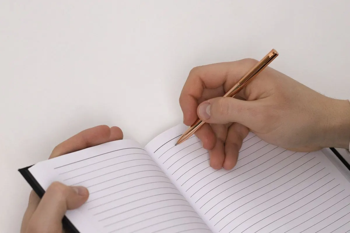Hands writing in a blank lined notebook