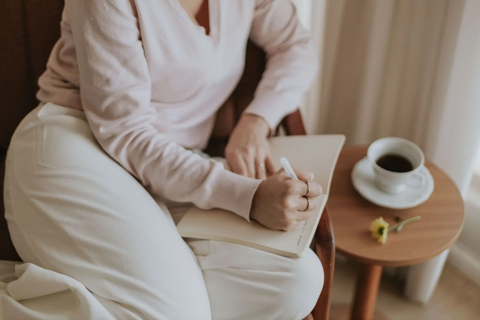 A person journaling in a cozy room with a cup of coffee beside them