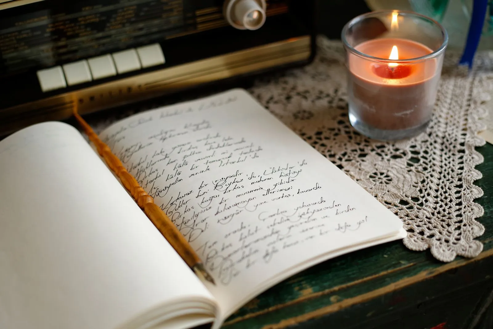 A handwritten notebook and pen beside a lit candle in warm, dim light