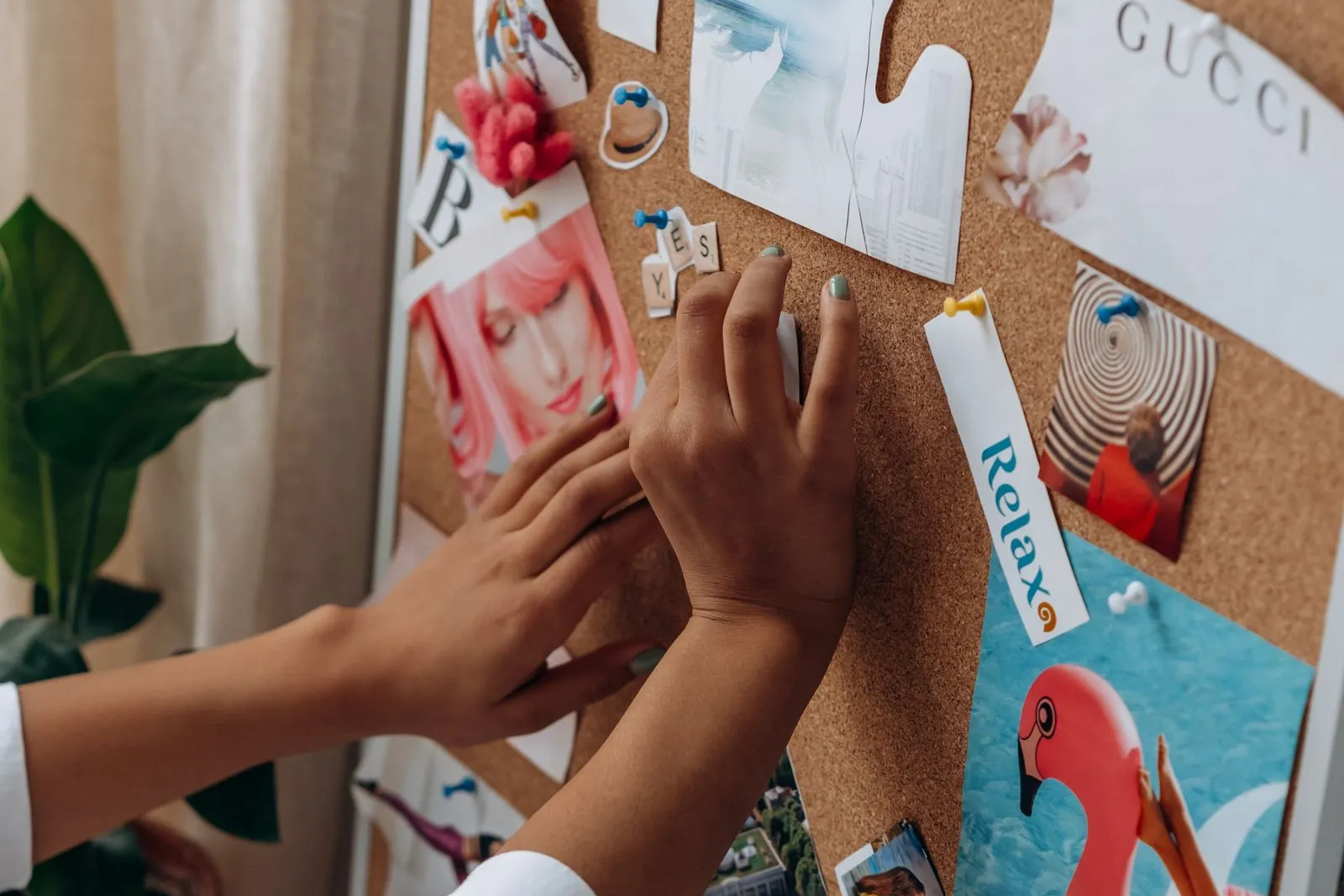 A hand pinning magazine cut-outs onto a cork vision board