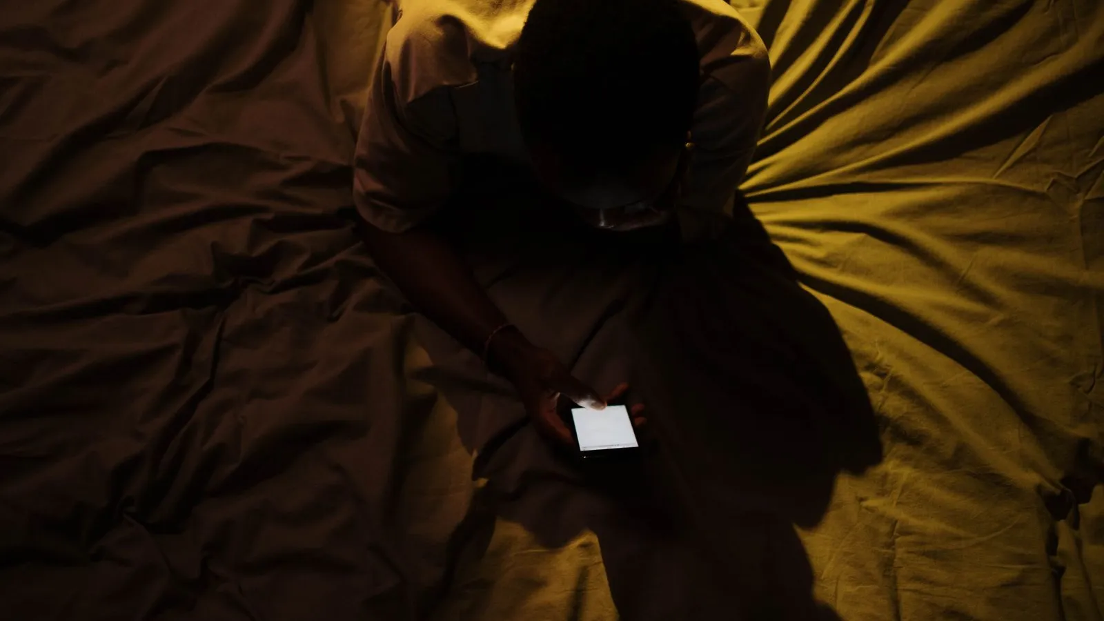 Person lying in bed scrolling on a smartphone in a dark room